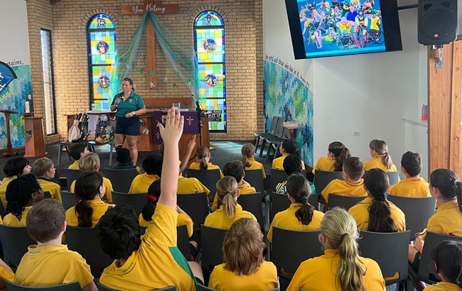A room full of children watch a presentation by a Para-athlete. A child raises their hand to ask a question.||A room full of children watch a presentation by a Para-athlete. A child raises their hand to ask a question.||