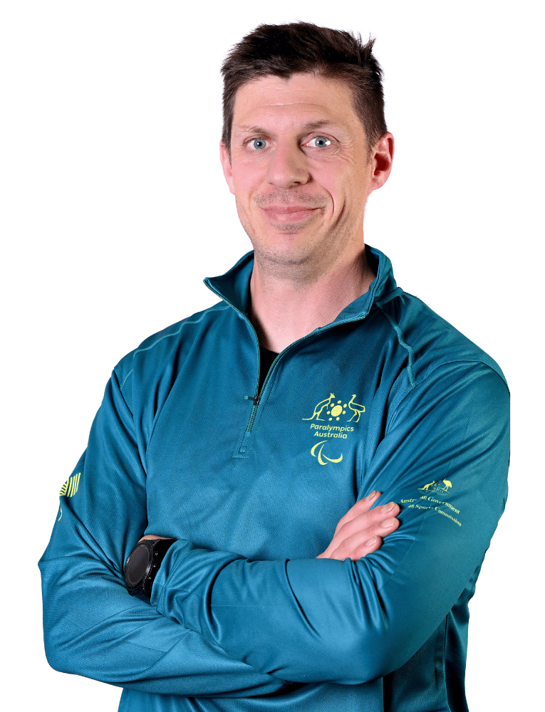 Portrait of a man smiling with arms crossed, wearing a teal athletic jacket with Paralympics Australia logo.