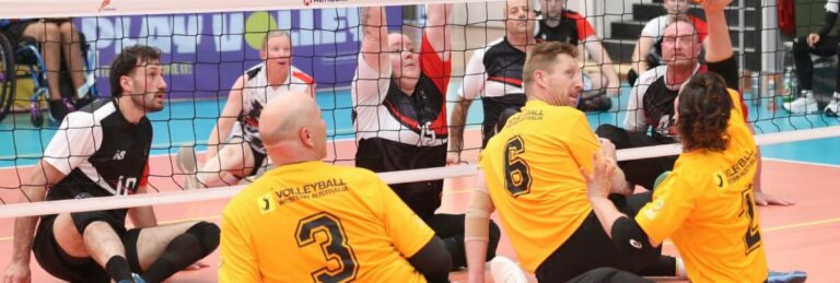 Volleyball match in progress; two yellow-jersey players (#3 and #6) on the floor near the net with black uniforms nearby.