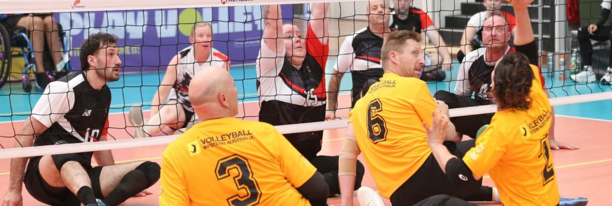 Volleyball match in progress; two yellow-jersey players (#3 and #6) on the floor near the net with black uniforms nearby.