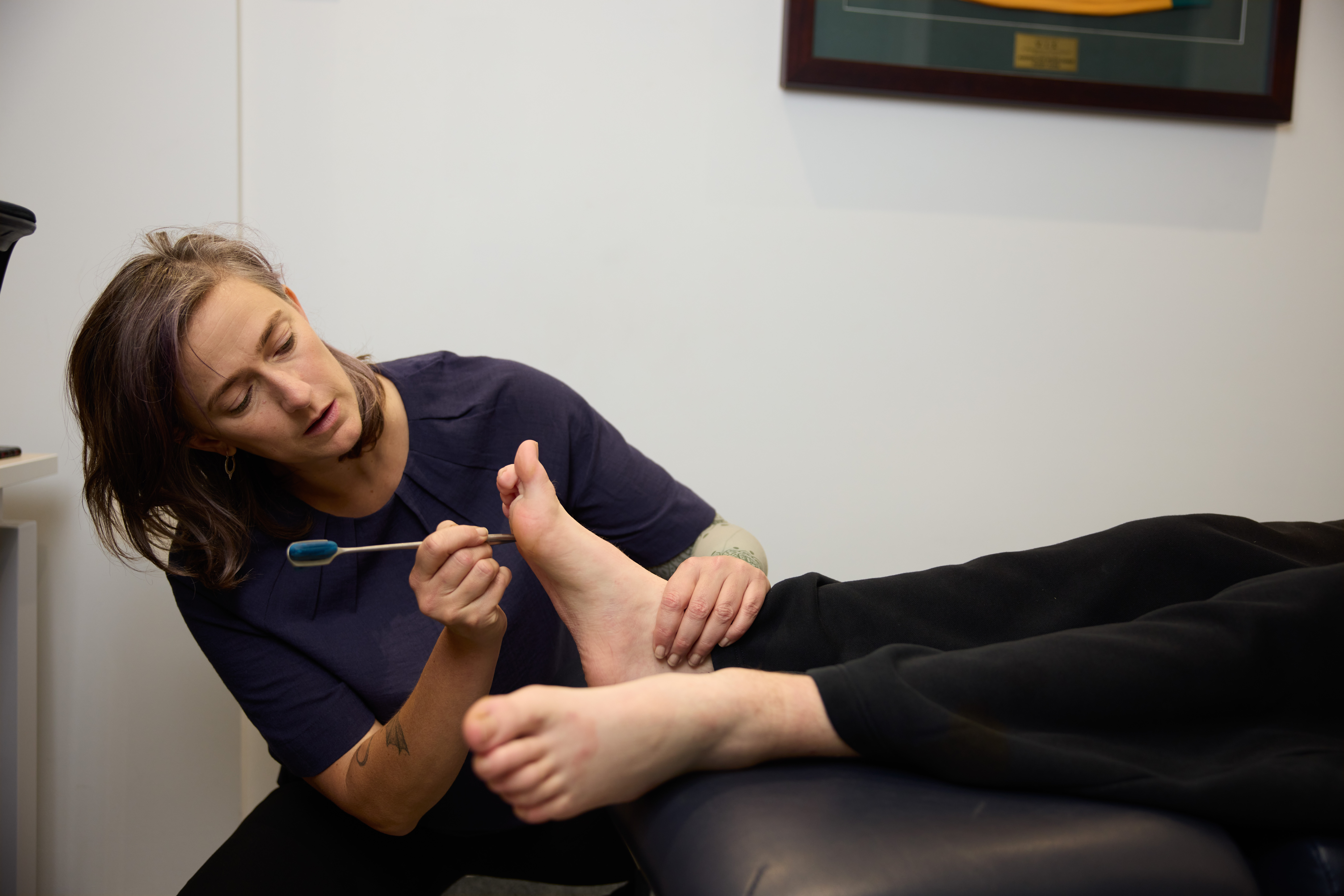 Practitioner using a tool to test sensivity on a client's foot while client lies down